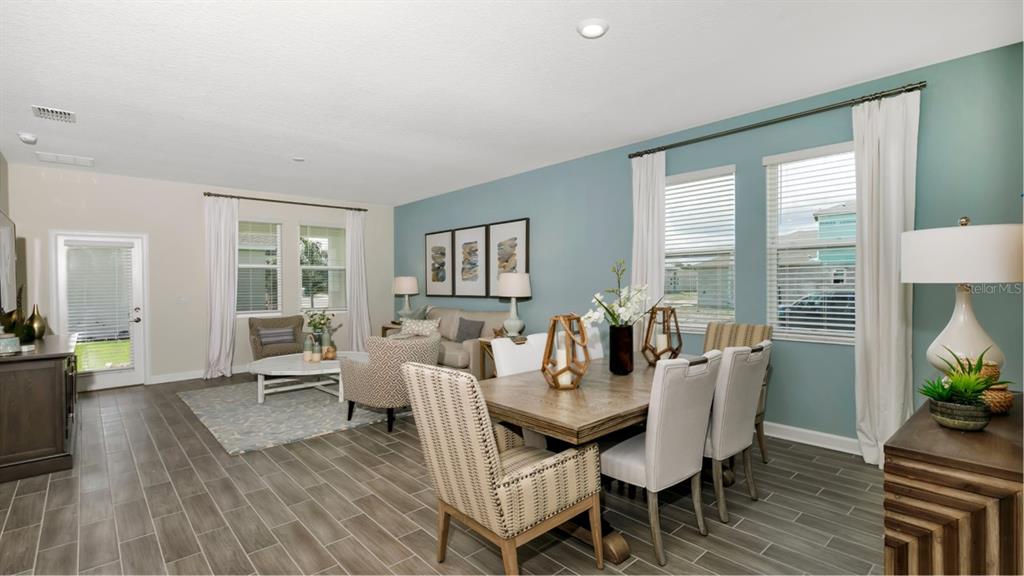 An open-concept living and dining area features blue accent walls, tile flooring, and large windows — 3273 WHOLENESS WAY, CLERMONT, FL