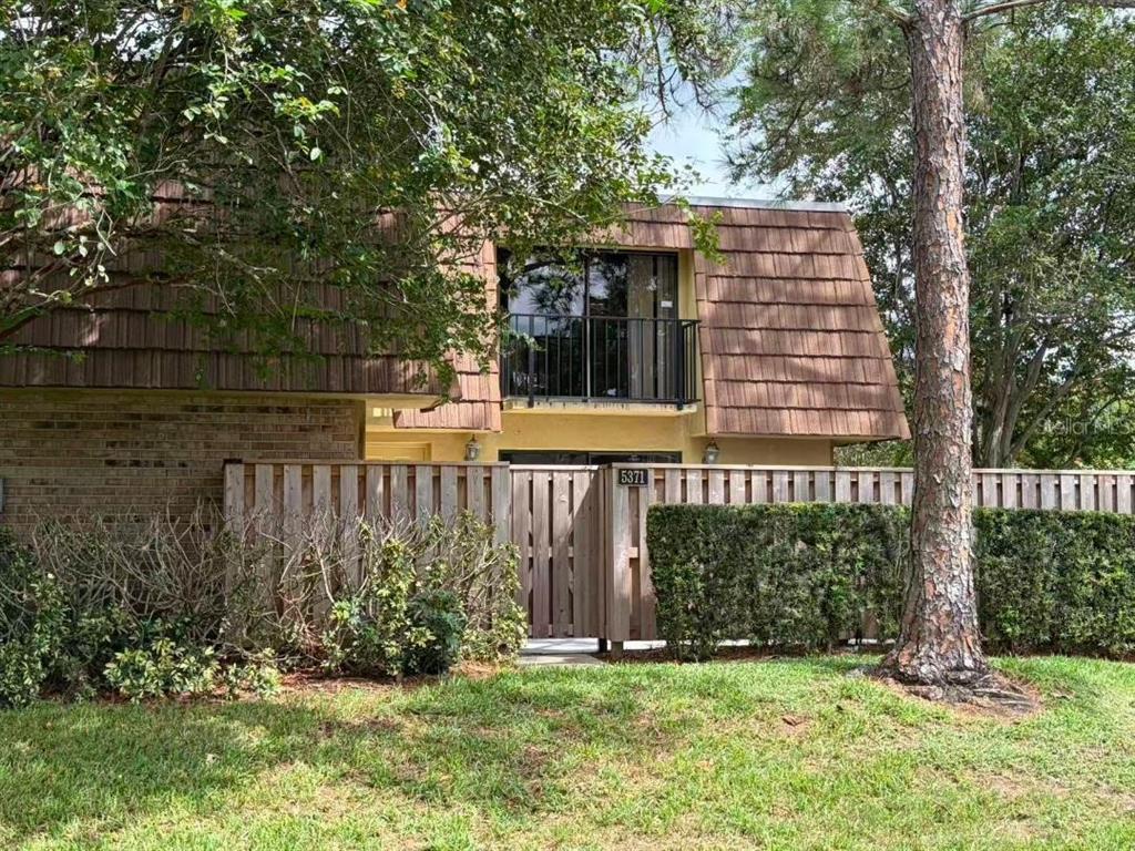Exterior view of a two-story townhouse with a paved patio, balconies, and sliding glass doors — 5371 BAMBOO COURT UNIT 401, ORLANDO, FL