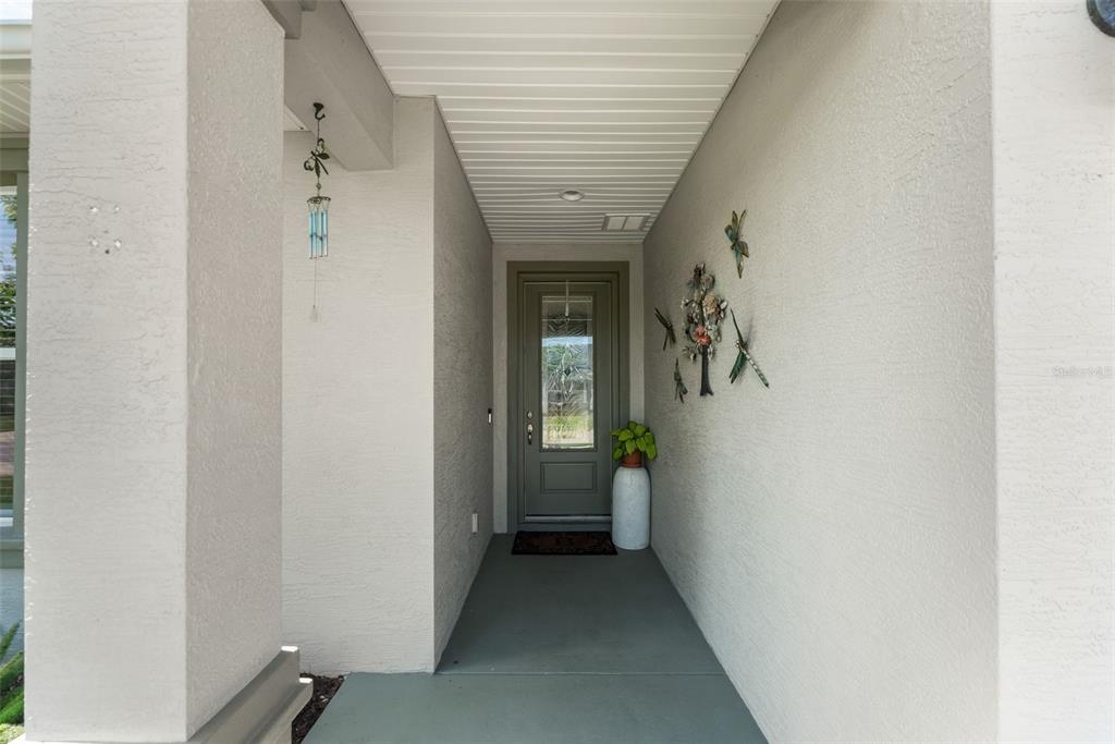 A covered entryway features a gray front door, a potted plant, and wall-mounted metal decorations — 5662 NW 40TH PL, OCALA, FL