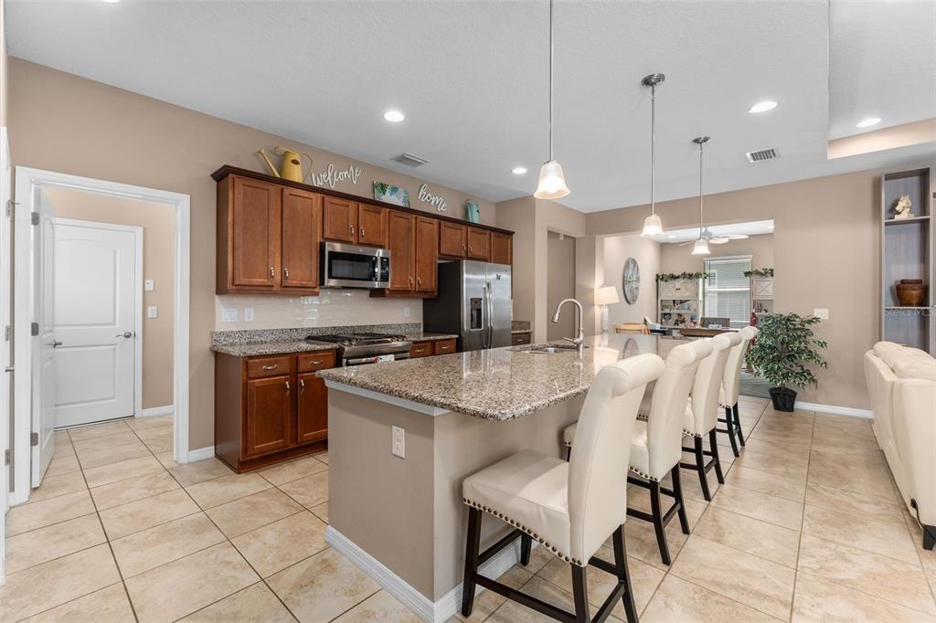 A kitchen features wood cabinets, granite countertops, a large island with seating, and tile flooring — 5662 NW 40TH PL, OCALA, FL