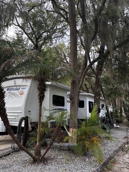 A white Wildwood travel trailer is parked on a gravel lot among trees and palms — 25367 140TH STREET NE UNIT 315, FORT MC COY, FL