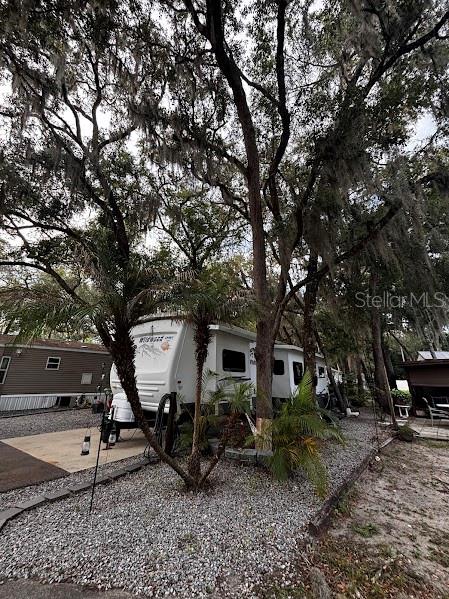 A white travel trailer is parked on a gravel lot beneath large, moss-draped oak trees — 25367 140TH STREET NE UNIT 315, FORT MC COY, FL