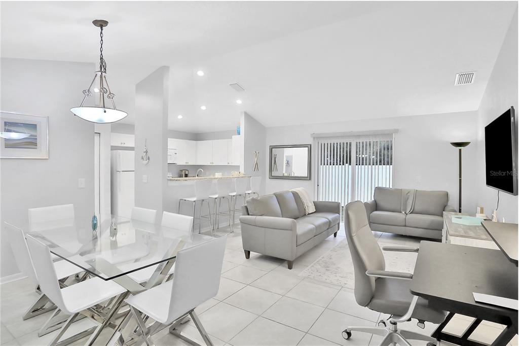 An open-concept living and dining area features white tile floors, gray furniture, and a kitchen — 1004 42ND TERRACE E, BRADENTON, FL