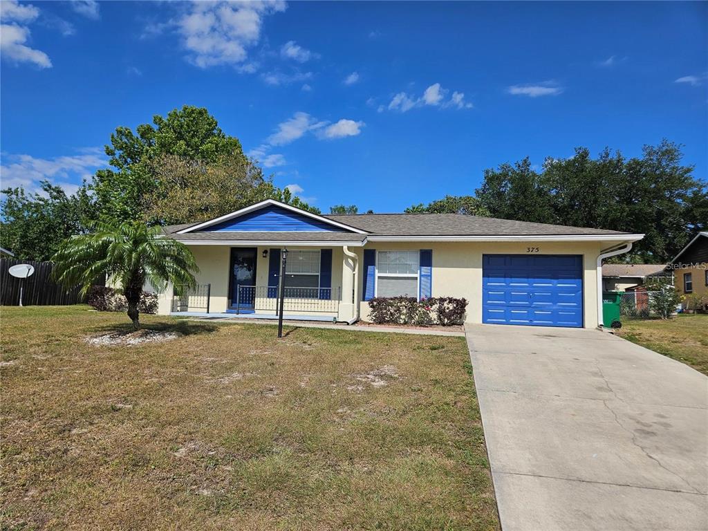 A single-story house with a blue garage door, blue shutters, and a palm tree — 375 WILLOW SONG COURT, EUSTIS, FL