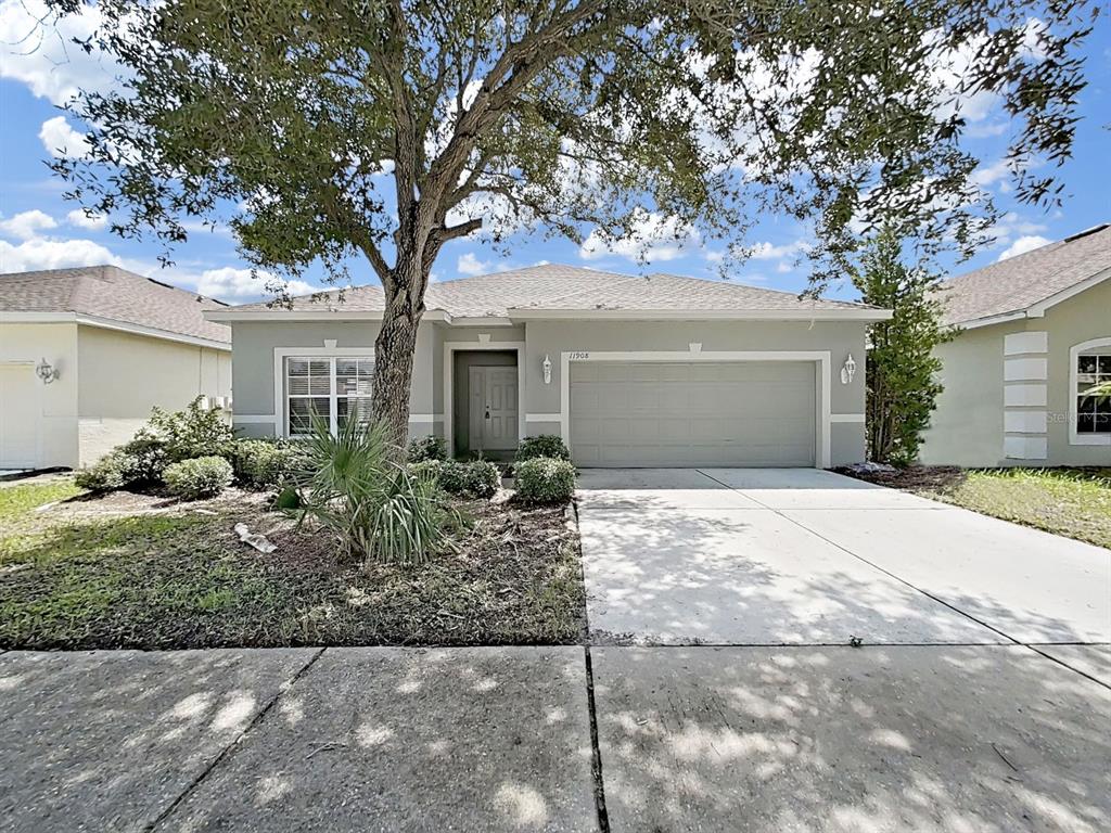 A single-story gray house with a two-car garage and a large tree in the yard — 11908 FERN BLOSSOM DRIVE, GIBSONTON, FL