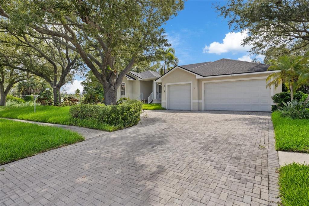A beige house with a three-car garage and a paved driveway sits under large trees — 2706 SKIMMER POINT DRIVE S, GULFPORT, FL