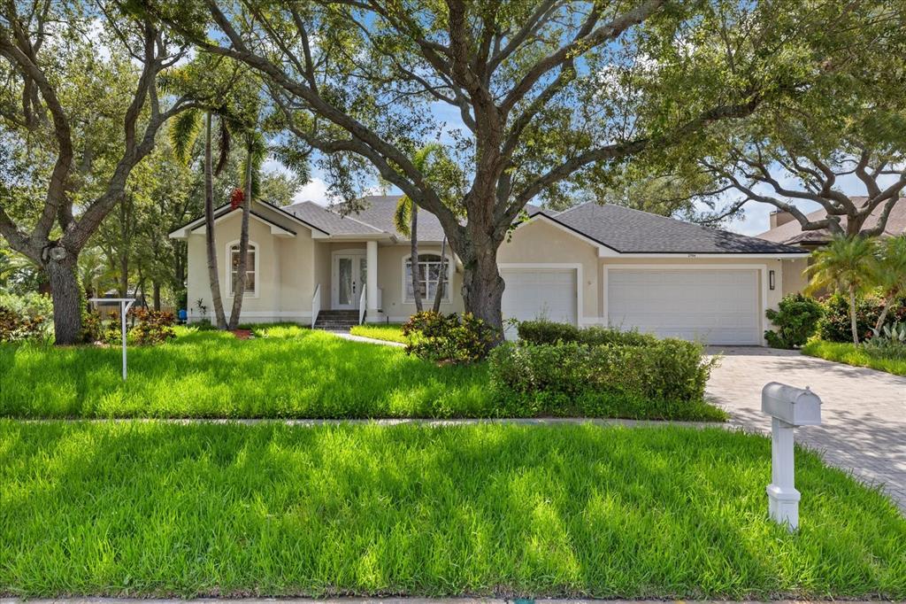 A single-story house with a beige stucco exterior, a two-car garage, and large oak trees — 2706 SKIMMER POINT DRIVE S, GULFPORT, FL