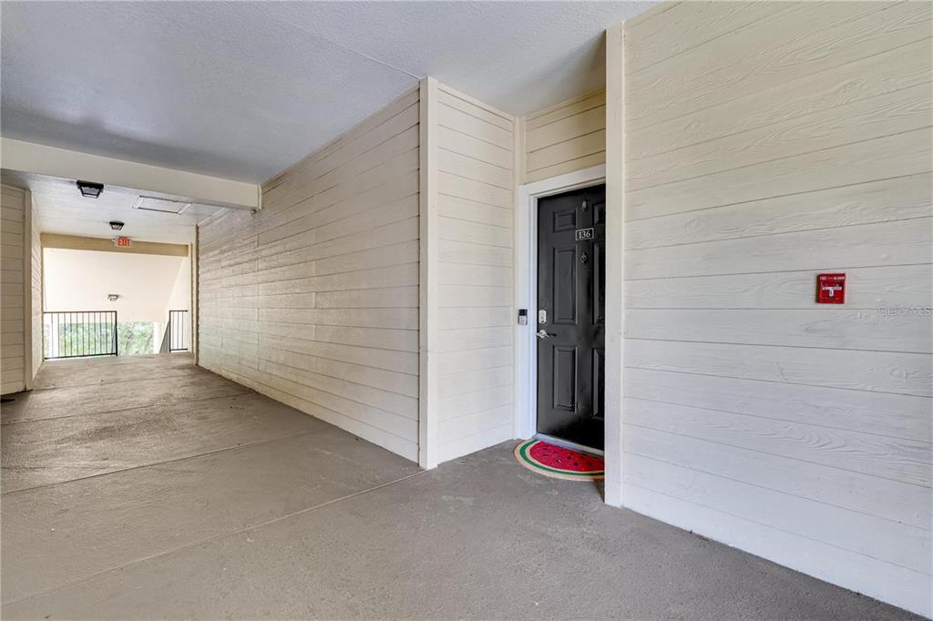 A black front door with a watermelon-shaped mat sits in a covered outdoor hallway — 2632 ROBERT TRENT JONES DRIVE UNIT 136, ORLANDO, FL