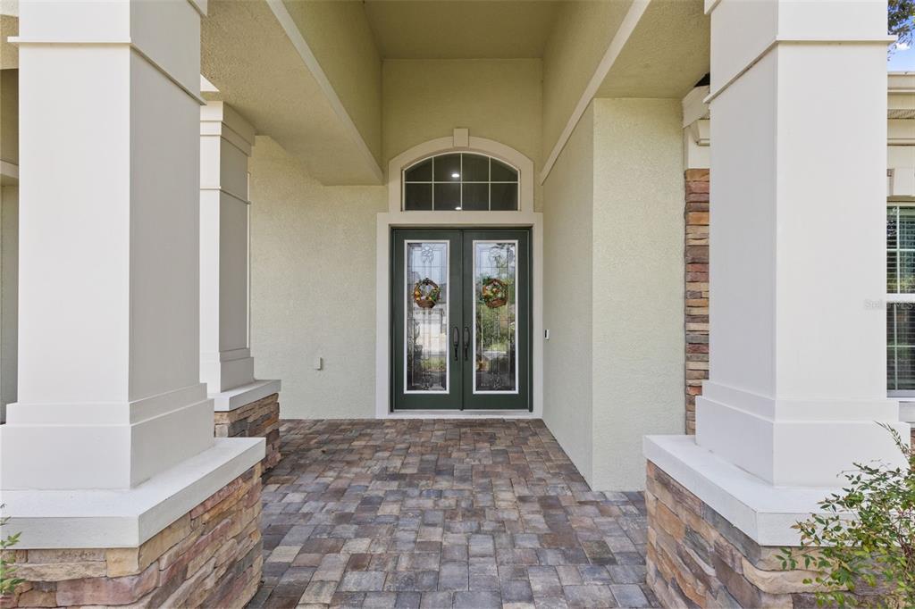 A covered entryway features a paver floor, stone-based columns, and a double glass-paneled front door — 27816 COBALT LANE, WESLEY CHAPEL, FL