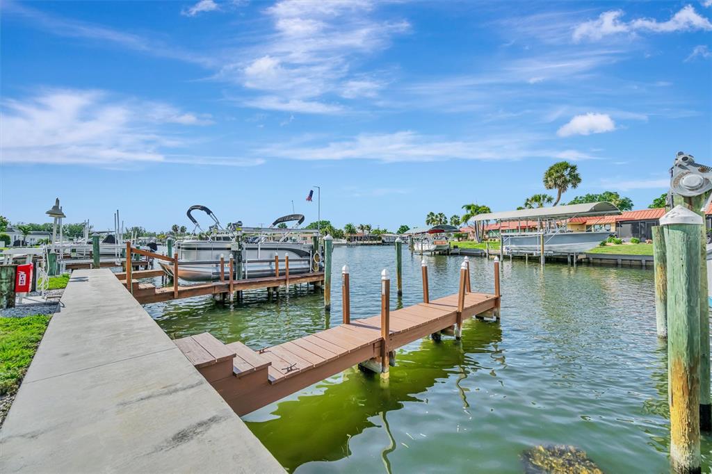A concrete dock leads to a wooden pier extending into a canal with moored boats — 9604 CORTEZ ROAD W UNIT 334, BRADENTON, FL