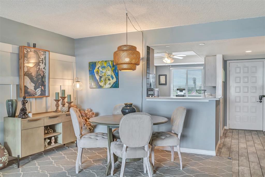 A dining area features a round table, upholstered chairs, a woven pendant light, and sideboard — 9604 CORTEZ ROAD W UNIT 334, BRADENTON, FL