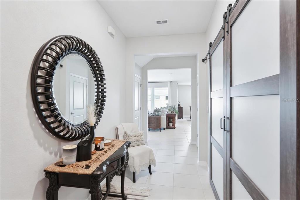 A bright entryway features a dark wood console table, a round mirror, and sliding barn doors — 13055 WILLOW GROVE DRIVE, RIVERVIEW, FL