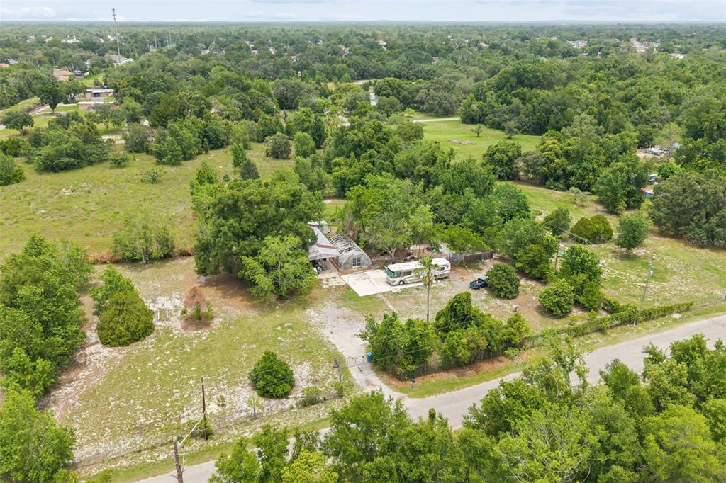 An aerial view shows a rural property with a house, greenhouse, and RV on land — 9345 ORCHARD WAY, SPRING HILL, FL
