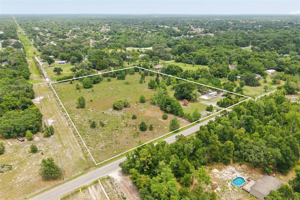 An aerial view shows a large, grassy, rectangular lot outlined in white near a road — 9345 ORCHARD WAY, SPRING HILL, FL