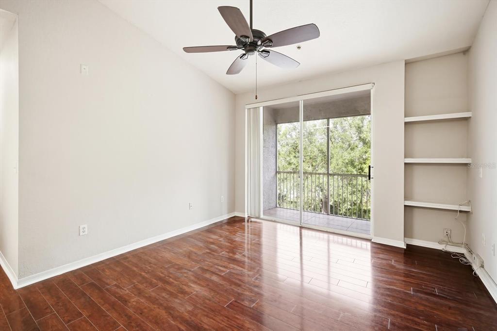 An empty room with wood-look flooring, a ceiling fan, built-in shelves, and a sliding glass door — 5703 LEGACY CRESCENT PLACE UNIT 301, RIVERVIEW, FL
