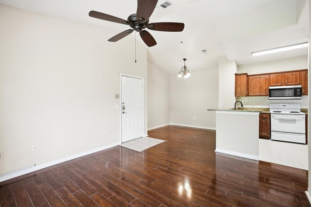 An open-concept living area with dark wood flooring, a ceiling fan, and an adjacent kitchen — 5703 LEGACY CRESCENT PLACE UNIT 301, RIVERVIEW, FL