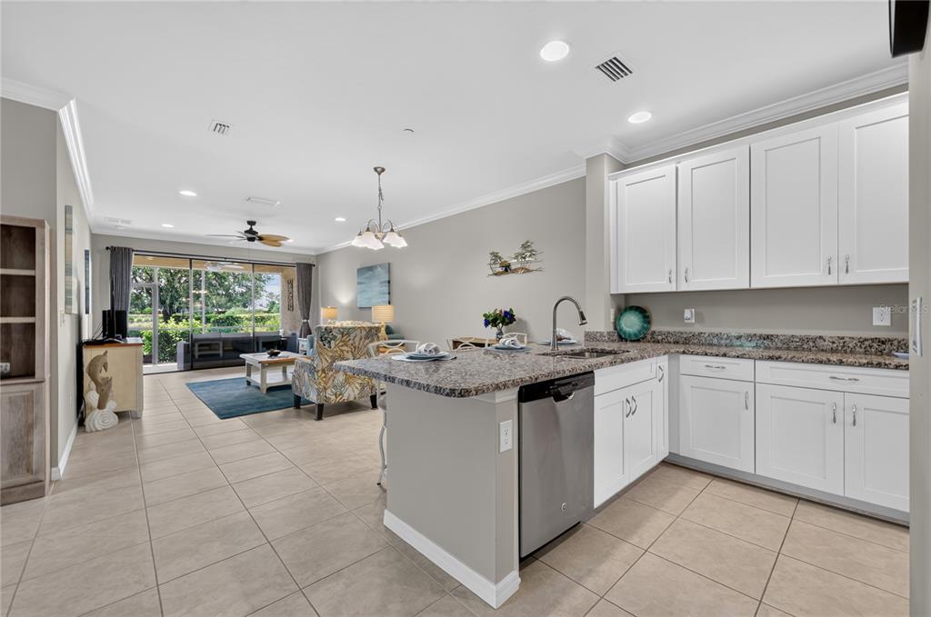 A kitchen with white cabinets and granite countertops opens into a living area with tile floors — 12710 SORRENTO WAY UNIT 101, BRADENTON, FL