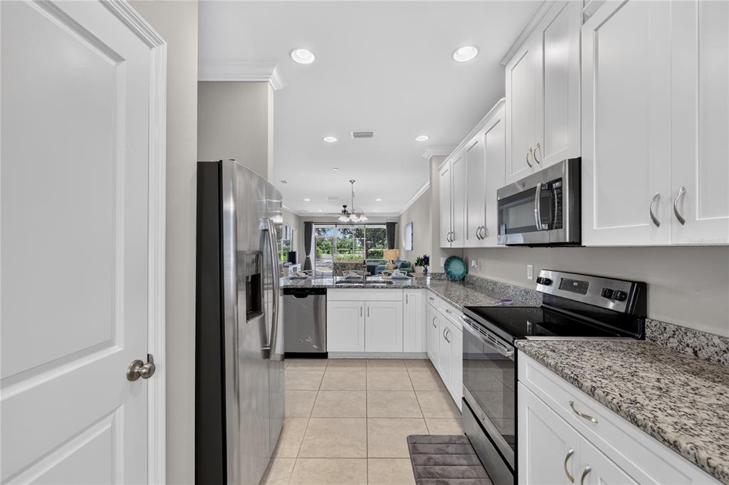 A galley-style kitchen features white cabinets, granite countertops, stainless steel appliances, and tile flooring — 12710 SORRENTO WAY UNIT 101, BRADENTON, FL