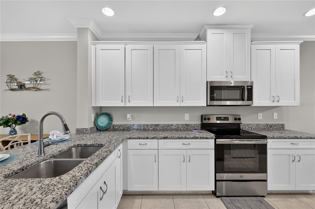 A kitchen features white cabinets, granite countertops, stainless steel appliances, and a double-basin sink — 12710 SORRENTO WAY UNIT 101, BRADENTON, FL