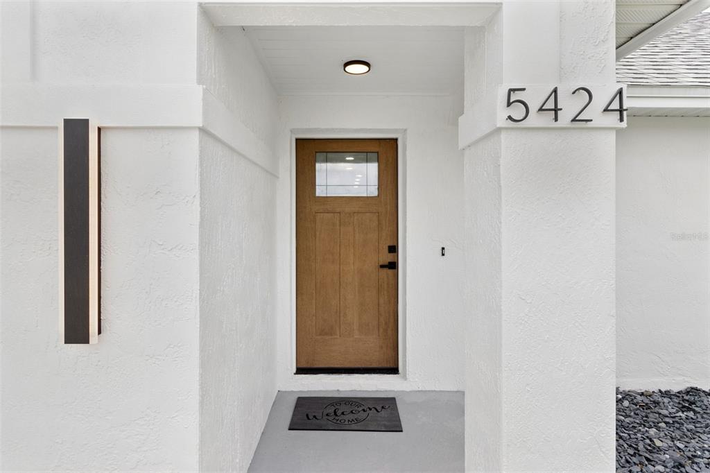 A front entryway features a wooden door, a welcome mat, and the house number 5424 — 5424 LOMA VISTA DRIVE E, DAVENPORT, FL