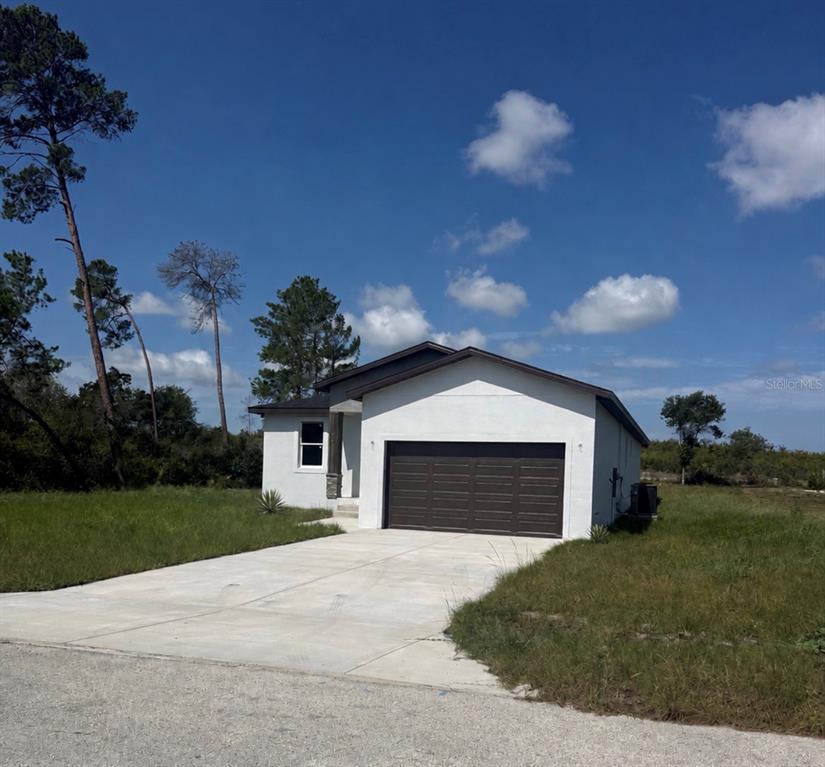 A single-story house with a white exterior, a dark garage door, and a concrete driveway — 5541 MOONGATE ROAD, SPRING HILL, FL