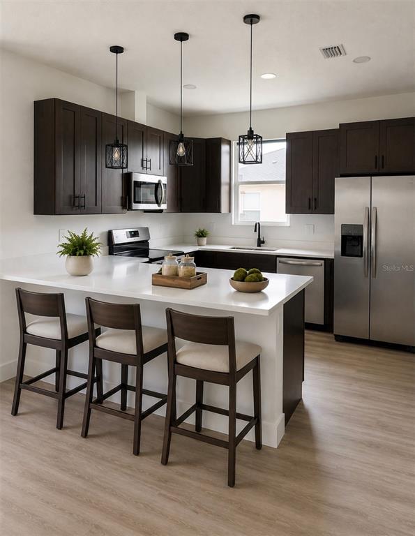 A modern kitchen features dark wood cabinets, a white island with three stools, and stainless appliances — 5541 MOONGATE ROAD, SPRING HILL, FL