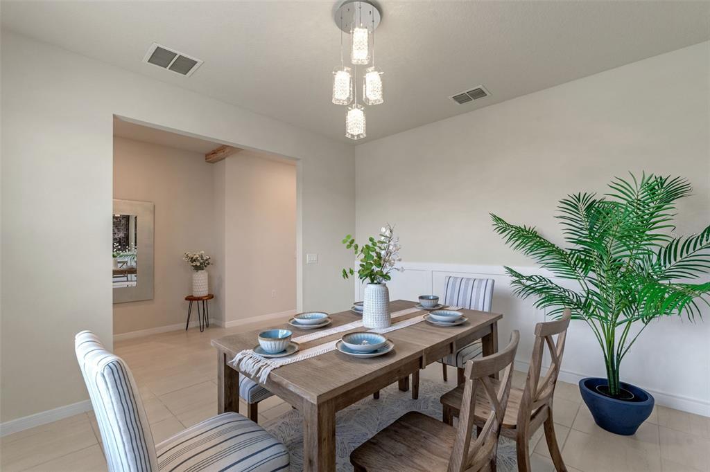 A dining room features a wooden table, striped chairs, a modern chandelier, and a potted plant — 17319 MILLION LAKES COURT, CLERMONT, FL