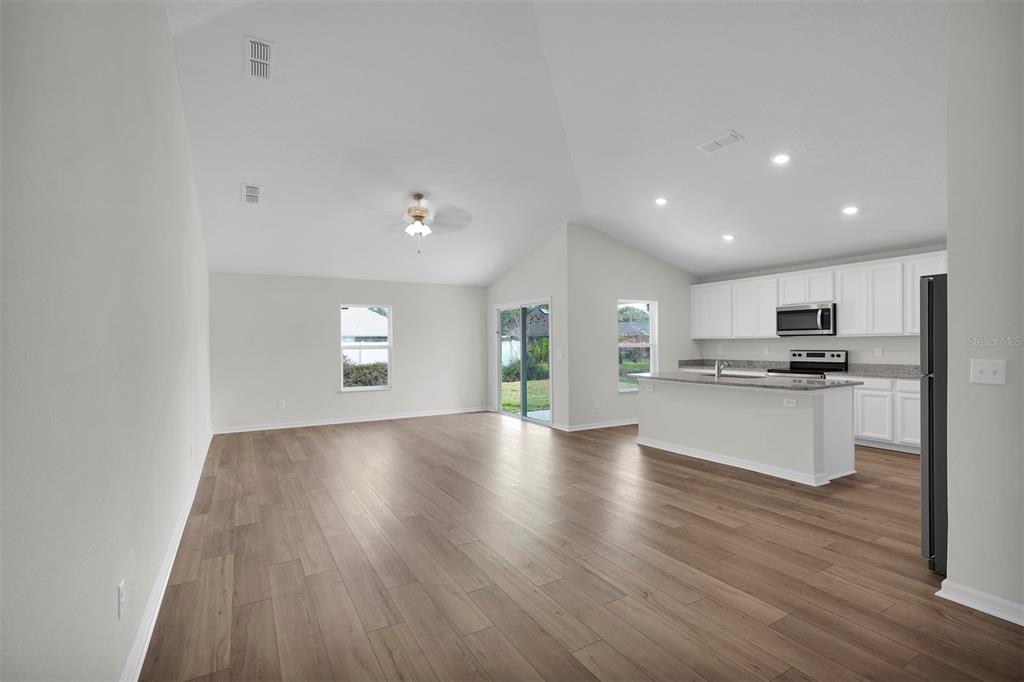 An open-concept living area features vaulted ceilings, wood-look flooring, and a kitchen with white cabinetry — 19 PINEAPPLE DRIVE, PALM COAST, FL