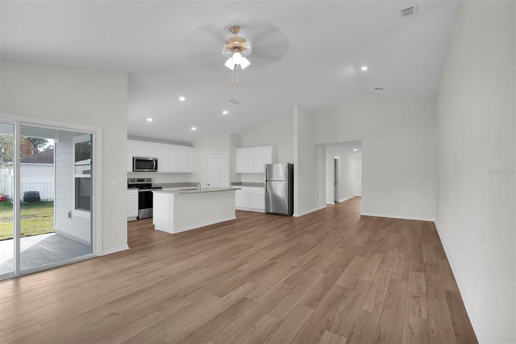 An open-concept kitchen and living area featuring wood-look flooring, white cabinetry, and stainless appliances — 19 PINEAPPLE DRIVE, PALM COAST, FL