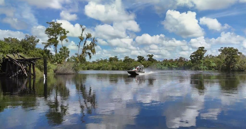 An airboat travels on a river near a wooden structure under a cloudy blue sky — SW AURIN GRADE UNIT A, ARCADIA, FL