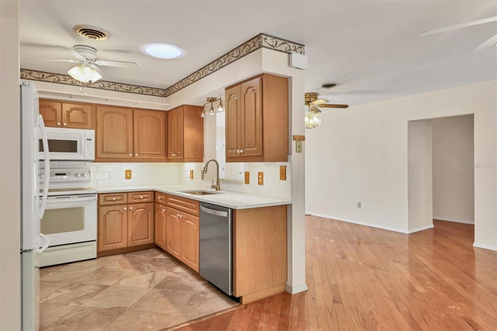 A kitchen with wood cabinets, white appliances, and tile flooring opens to a hardwood-floored room — 1120 GRAHAM ROAD, VENICE, FL