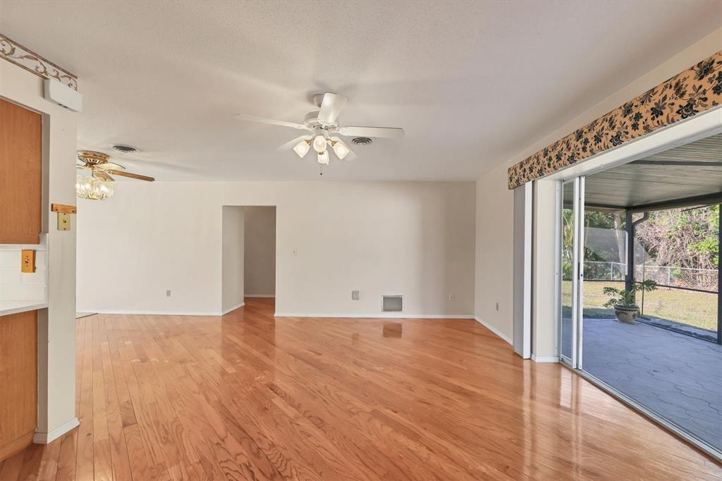 An open living area features hardwood floors, a ceiling fan, and sliding glass doors to a patio — 1120 GRAHAM ROAD, VENICE, FL