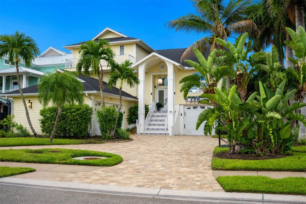 A yellow two-story house features a white front door, stairs, and a paved driveway — 255 46TH AVENUE, ST PETE BEACH, FL