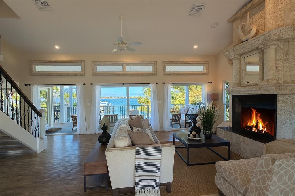 A living room with a stone fireplace, wood floors, and sliding doors overlooking the water — 255 46TH AVENUE, ST PETE BEACH, FL