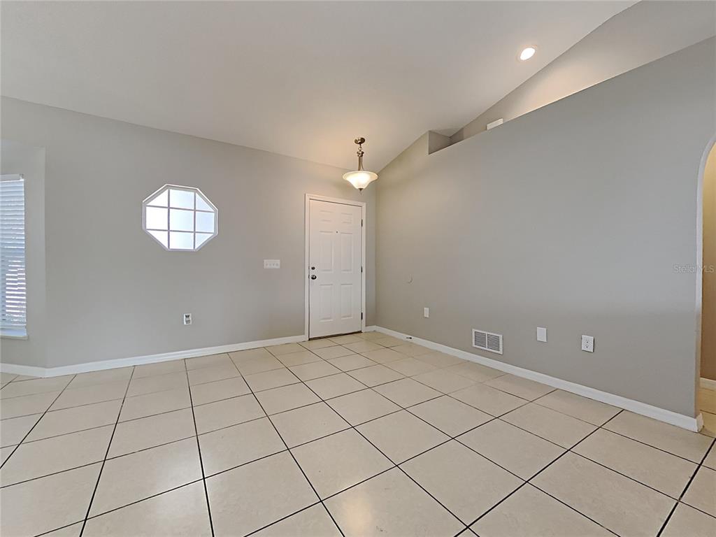 An empty room with light-colored tile flooring, gray walls, a vaulted ceiling, and an entryway door — 1322 DRAGON HEAD DRIVE, VALRICO, FL