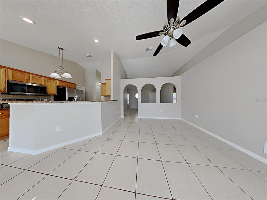 An open-concept kitchen and living area features tile flooring, arched wall cutouts, and a ceiling fan — 1322 DRAGON HEAD DRIVE, VALRICO, FL