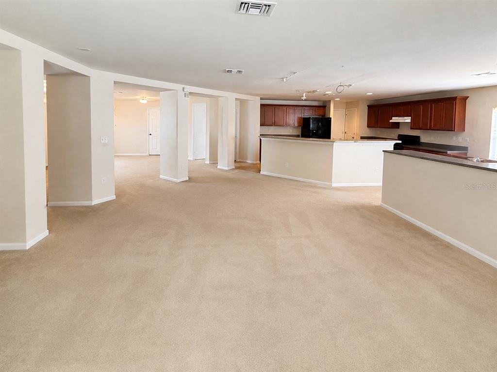 An open-concept living area features beige carpeting, white walls, and a kitchen with dark cabinetry — 21468 DAWSON AVENUE, PORT CHARLOTTE, FL