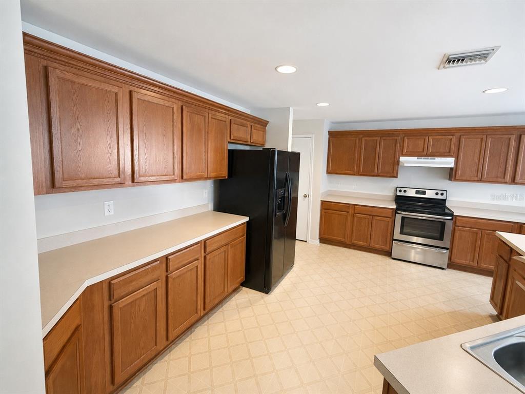 A kitchen features oak cabinets, beige countertops, a black refrigerator, and a stainless steel stove — 21468 DAWSON AVENUE, PORT CHARLOTTE, FL