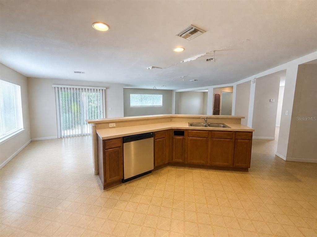 A kitchen with wood cabinets and a stainless steel dishwasher overlooks an open living area — 21468 DAWSON AVENUE, PORT CHARLOTTE, FL