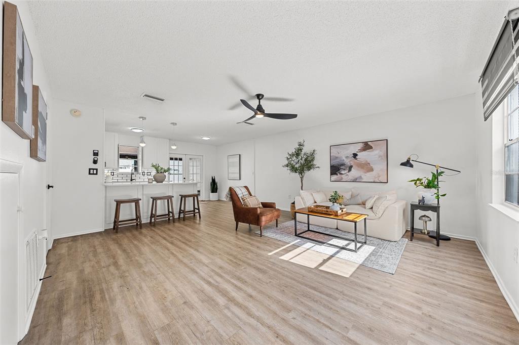 A bright living room features light wood-look flooring, a white sofa, and an open kitchen — 11917 CONGRESSIONAL DRIVE, TAMPA, FL