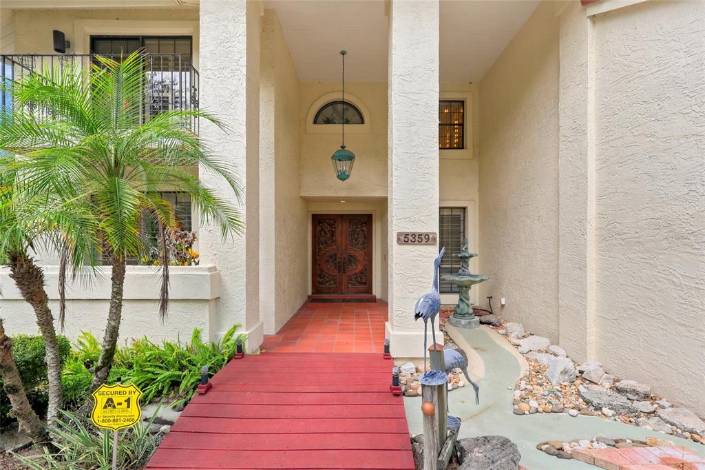 A red wooden bridge leads to the double front doors of a stucco house — 5359 SADDLEBROOK WAY, WESLEY CHAPEL, FL