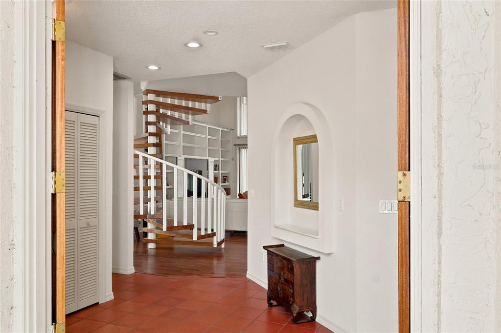 An entryway with terracotta tile flooring leads to a spiral staircase and a living area — 5359 SADDLEBROOK WAY, WESLEY CHAPEL, FL