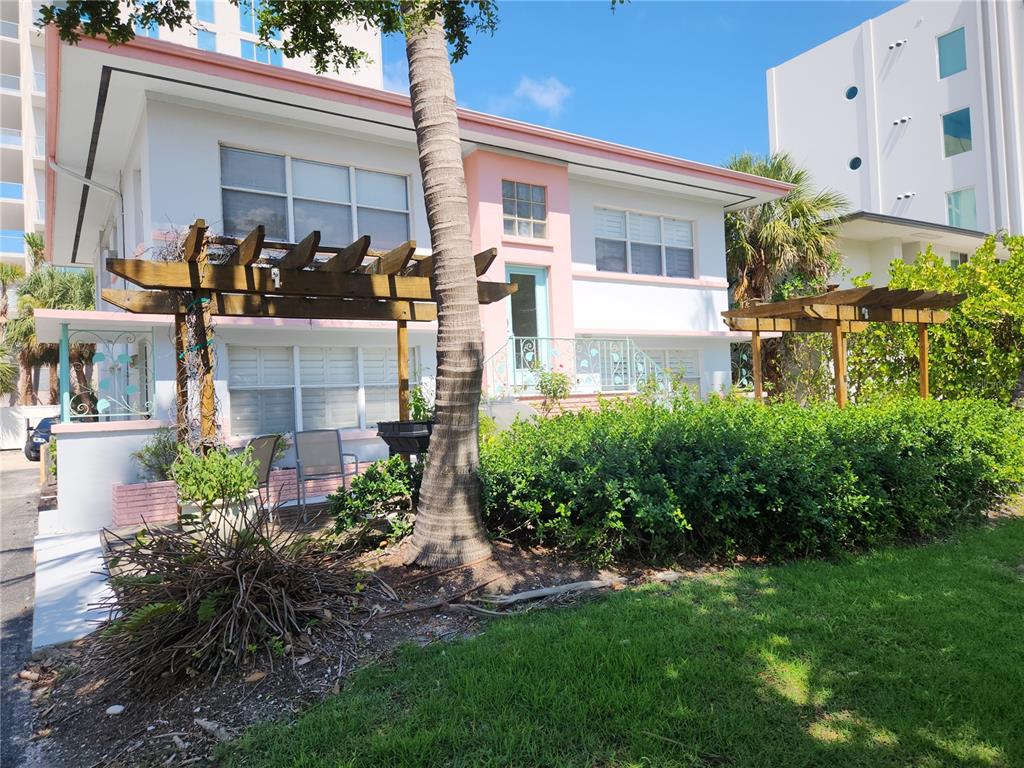 A two-story white building with pink trim features a wooden pergola and palm tree — 565 GOLDEN GATE POINT UNIT 1, SARASOTA, FL