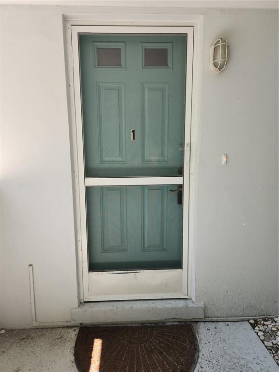 A teal storm door with the number one is mounted on a light gray exterior wall — 565 GOLDEN GATE POINT UNIT 1, SARASOTA, FL