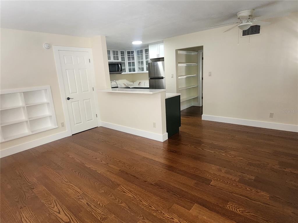 A living area with hardwood floors features a built-in bookshelf and an open kitchen pass-through — 565 GOLDEN GATE POINT UNIT 1, SARASOTA, FL