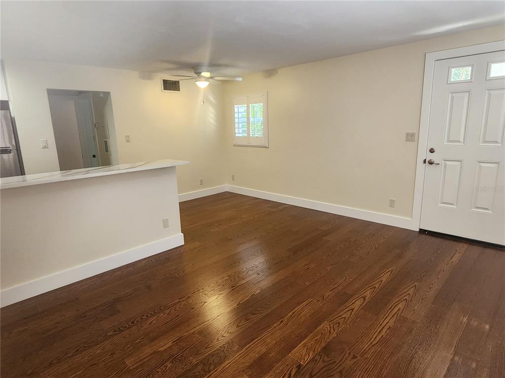 An interior view of a living area with hardwood floors, a kitchen counter, and door — 565 GOLDEN GATE POINT UNIT 1, SARASOTA, FL