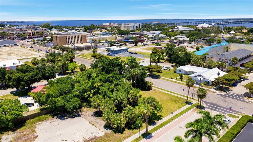 An aerial view shows a vacant lot with trees and surrounding commercial and residential buildings — 261 E OLYMPIA AVENUE, PUNTA GORDA, FL