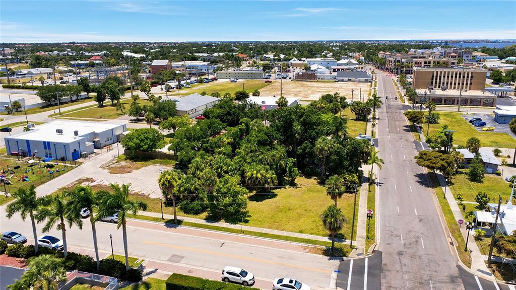 An aerial view shows a vacant lot surrounded by trees, commercial buildings, and a road — 261 E OLYMPIA AVENUE, PUNTA GORDA, FL