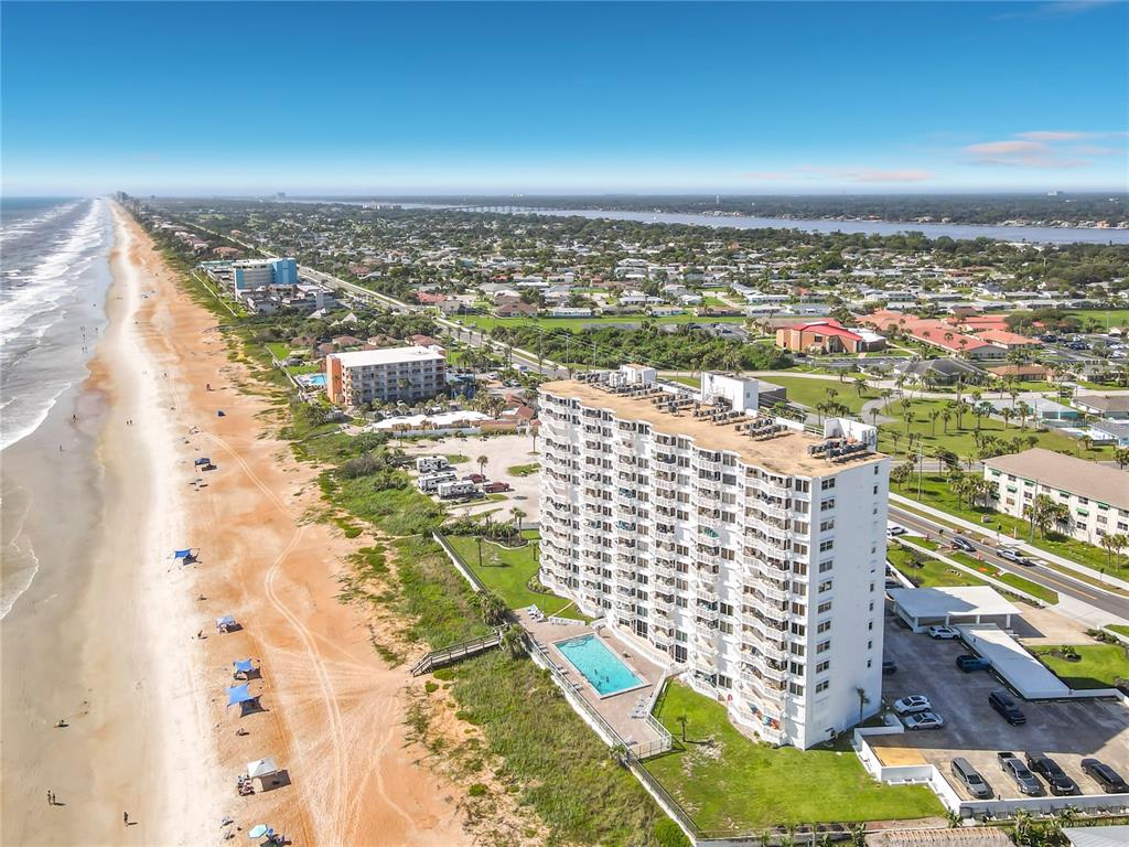 An aerial view shows a high-rise beachfront condominium building with a pool and parking lot — 1051 OCEAN SHORE BOULEVARD UNIT 304, ORMOND BEACH, FL
