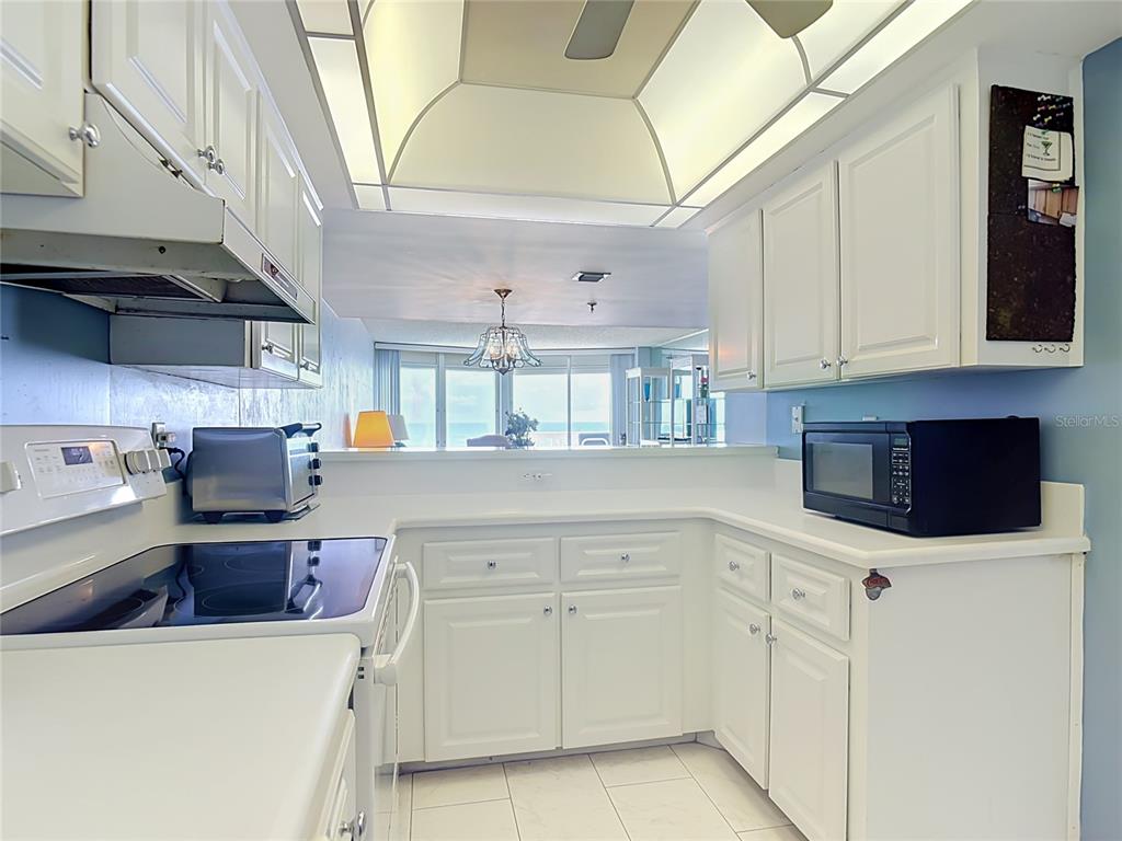 A white kitchen features cabinetry, a stove, a microwave, and a view into the living area — 1051 OCEAN SHORE BOULEVARD UNIT 304, ORMOND BEACH, FL